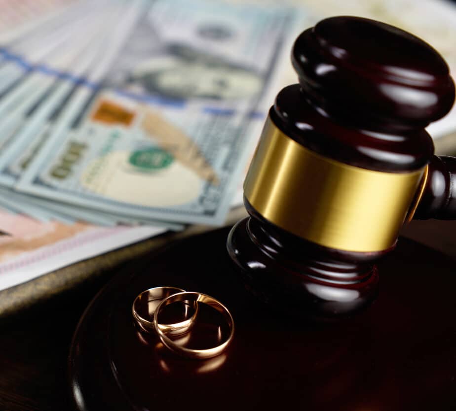 Close-up of wedding ring, judge gavel money dollar bills, marriage certificate, and a fountain pen in the background. Symbol of divorce settlement, alimony, asset division, or prenuptial agreements