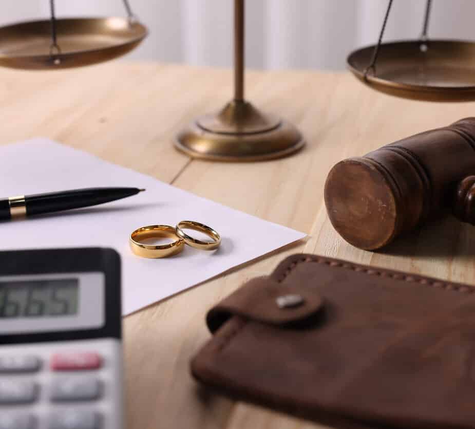 Alimony. Calculator, wallet, rings, sheet of paper, pen, gavel and scales on wooden table, closeup